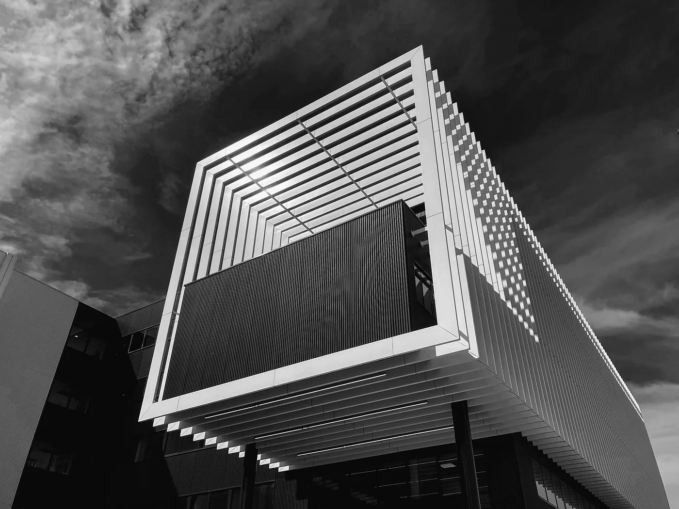 The Centre for Integrative Biology building in Toulouse, seen from below: a white slatted frame projecting over the entrance against a dark sky